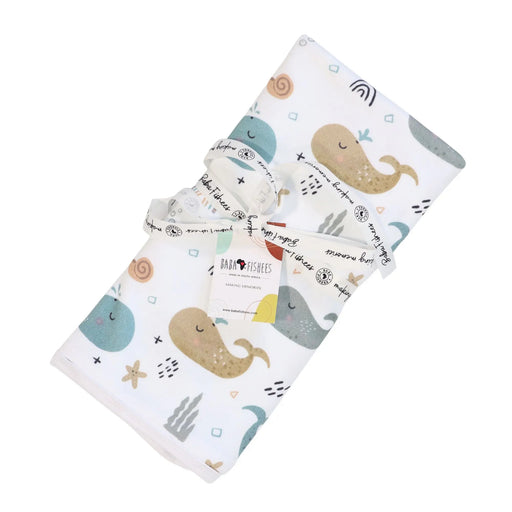 Baby blanket with whales on white background, featuring teal, sandy brown, and grey whale print rolled up with a ribbon.