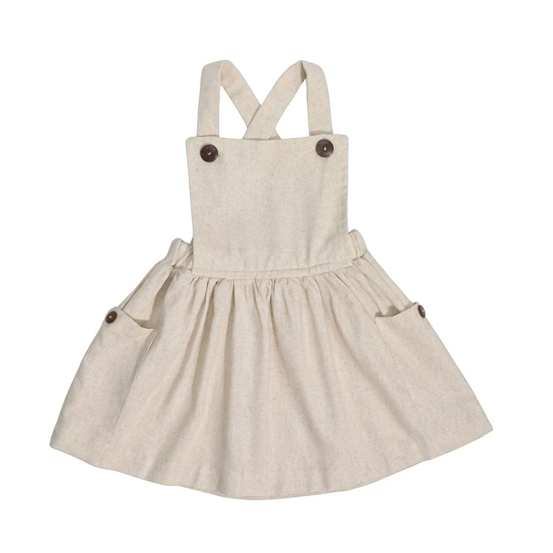 Natural linen dungaree dress with wooden buttons, gathered skirt, and cross-back straps.