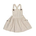 Natural linen dungaree dress with wooden buttons, gathered skirt, and cross-back straps.