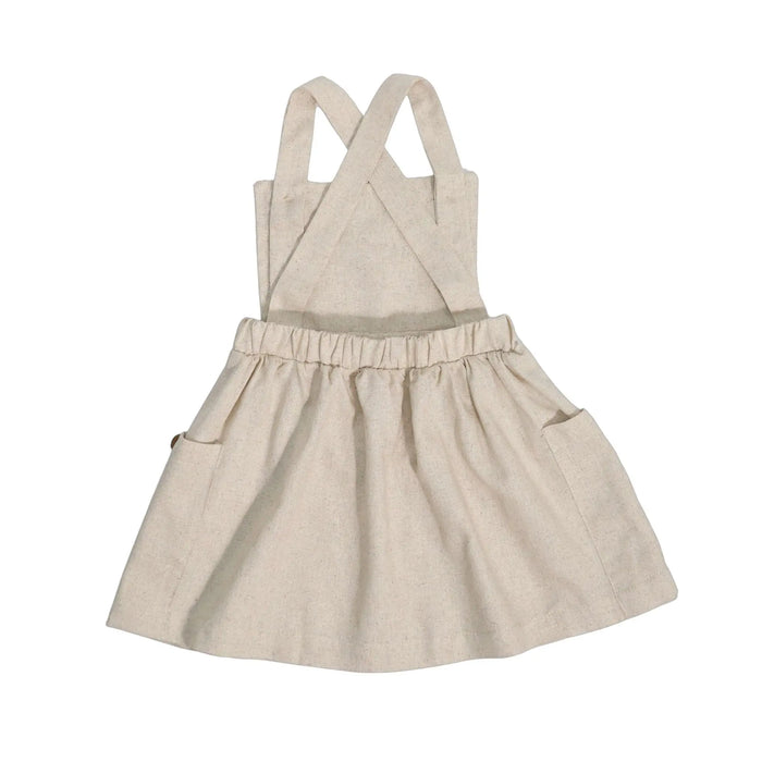 Back of natural linen dungaree dress with wooden buttons, gathered skirt, and cross-back straps.