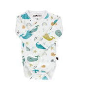 Front view of a white long-sleeve wrap-style baby onesie featuring a whimsical whale print in shades of blue, teal, and mustard, accented with rainbows, starfish, and seashells. Designed with press-stud closures for easy dressing.