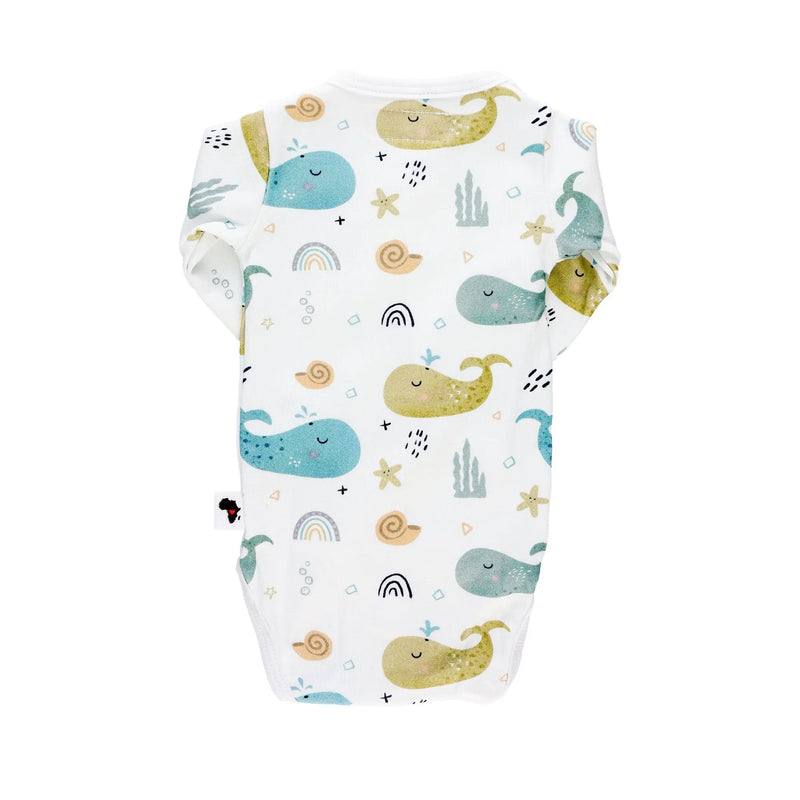 Back view of a white long-sleeve wrap-style baby onesie featuring a whimsical whale print in shades of blue, teal, and mustard, accented with rainbows, starfish, and seashells. Designed with press-stud closures for easy dressing.