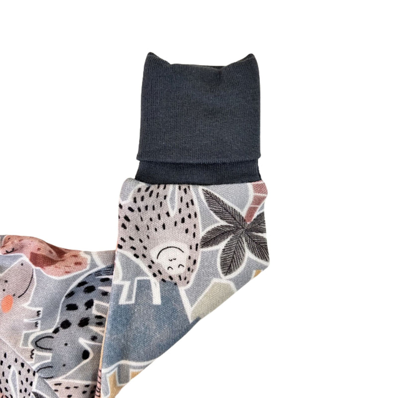 A close-up of a multicolor printed folded arm  with cartoon animals and leaves showining the mitten in airforce blue rib.