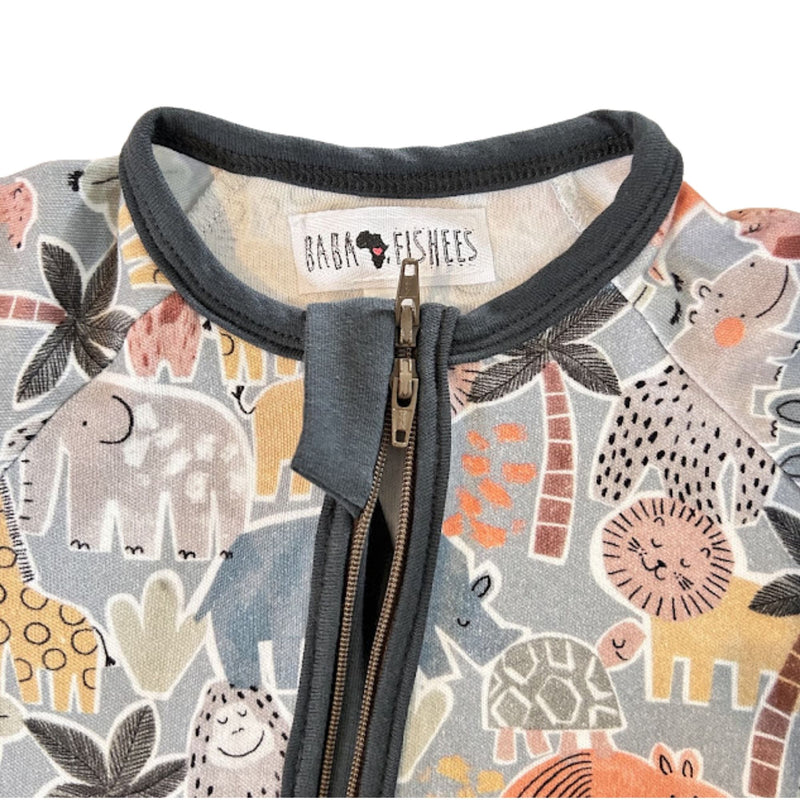 Close-up of an adapt romper baby zip-up garment with an airforce blue ribbed collar and zipper placket, featuring a colorful safari animal print including elephants, giraffes, lions, and palm trees. The inner label reads 'BABA FISHEES'.