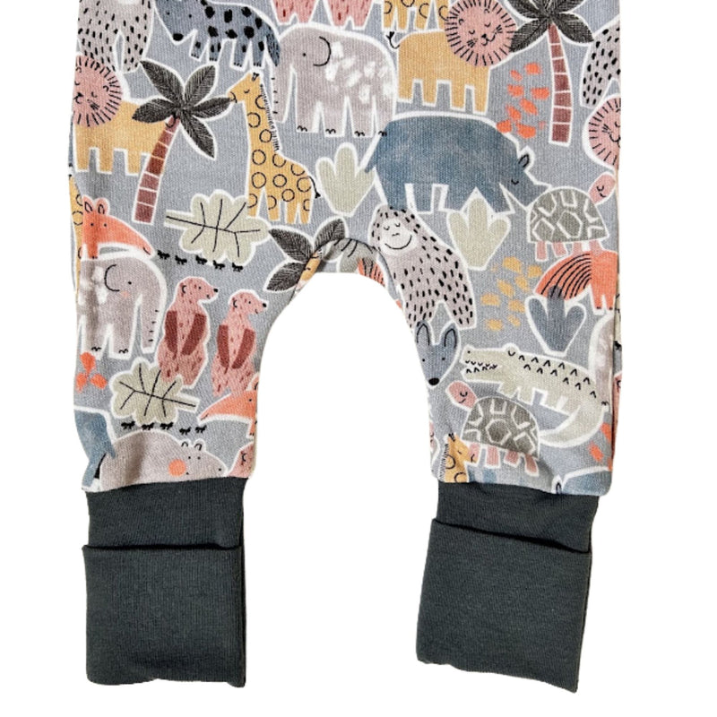 A closeup of the legs of the adapt romper - meerkat manor pair with an all-over safari animal print on a light gray background, featuring airforce blue ribbed cuffs at the bottom.
