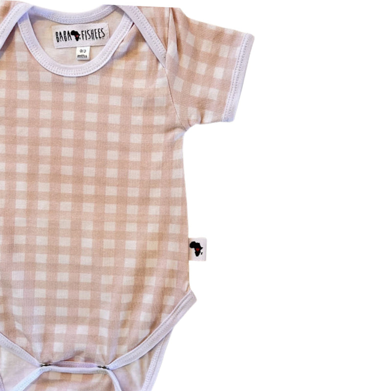 A short-sleeve baby bodysuit with a light pink and white gingham check pattern, featuring white ribbed trim and a visible 'BABA FISHEES' brand label.