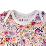 Close-up of the Floral Fantasy short-sleeve onesie’s envelope neckline, white binding and floral print detail