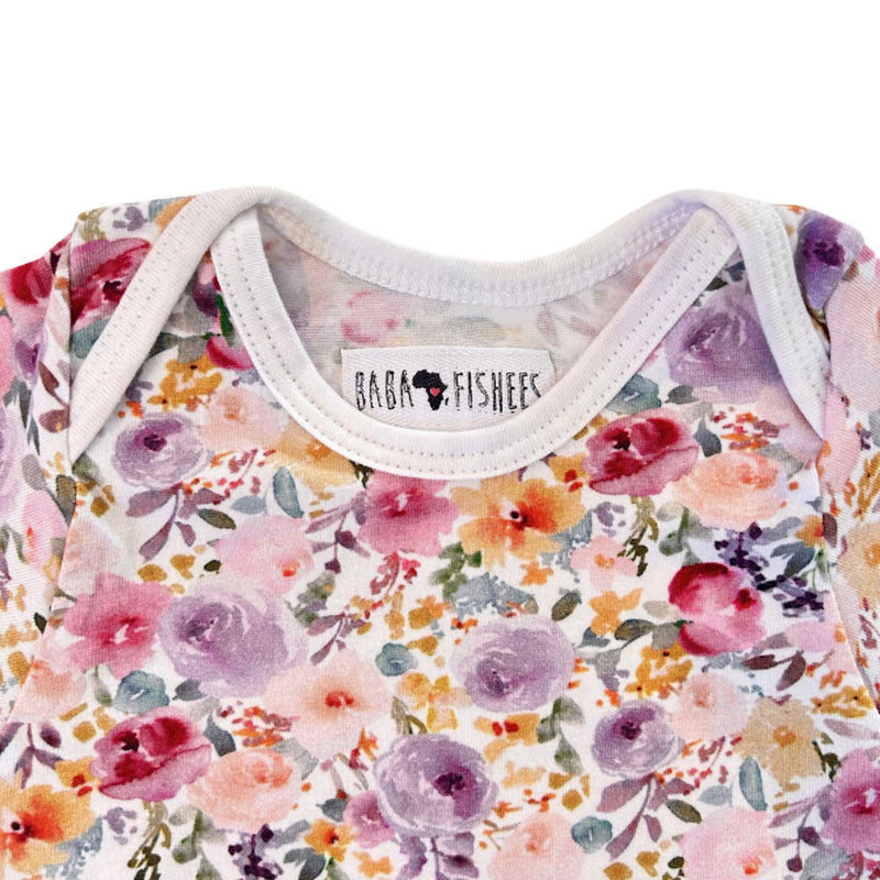 Close-up of the Floral Fantasy short-sleeve onesie’s envelope neckline, white binding and floral print detail