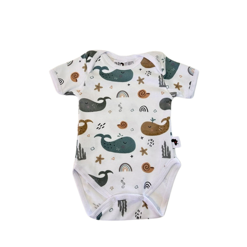 A front view of a short-sleeve white baby bodysuit with an all-over whimsical print of whales, starfish, rainbows, and seashells in mustard, blues and greys.