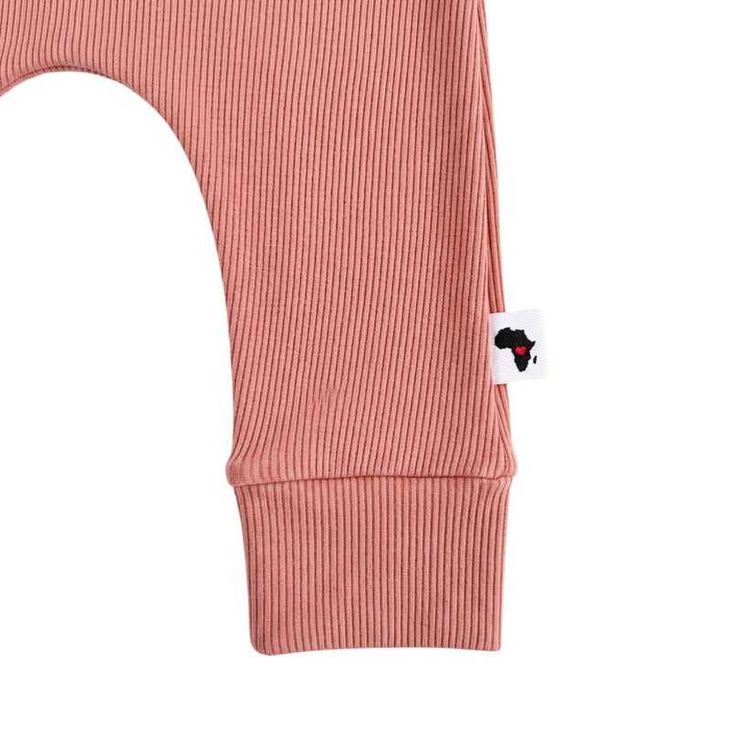 Close-up of a ribbed pink garment leg with a small white brand tag featuring a black silhouette of Africa with a red heart, shown on a white background.