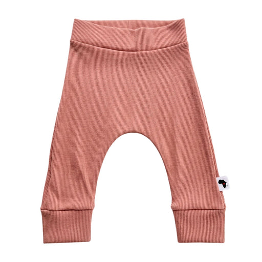 A pair of pink ribbed knit baby pants with an arched leg design, ribbed waistband, and ribbed ankle cuffs, featuring a small white tag with a black logo on the left ankle.