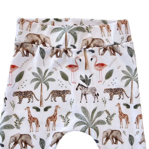 White baby cuff pants showing the waistband featuring a colorful safari animal print with giraffes, elephants, flamingos, zebras, leopards, palm trees, and leaves.