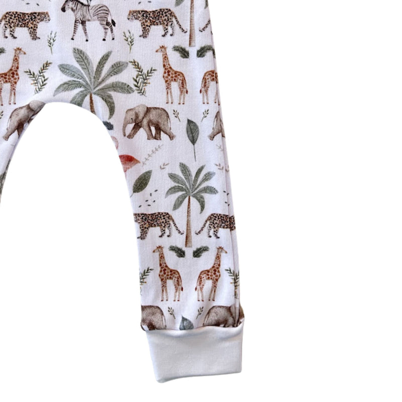 White children's leggings with an all-over safari animal print featuring giraffes, zebras, elephants, and palm trees, finished with a solid white ribbed cuff.