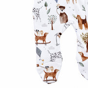 Close-up of the built-in footies on the Dogs Playground Footy Romper, showing brown dogs on skateboards, a spotted dog, trees, leaves and kite details on white cotton fabric.