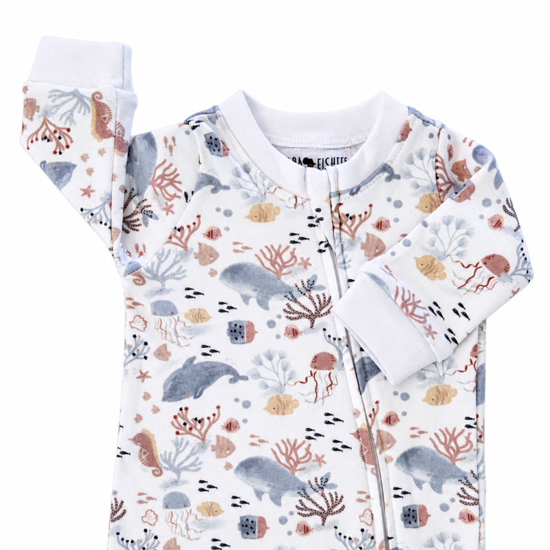 Finn and Friends footy romper neckline with white neckband, protective zip cover and white sleeve cuffs beside a pastel dolphin, fish and coral print.