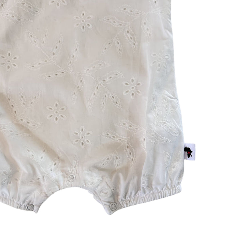 Close-up of the white romper’s lower section, showing three practical crotch press studs, elasticated leg openings and embroidered broderie anglaise fabric.