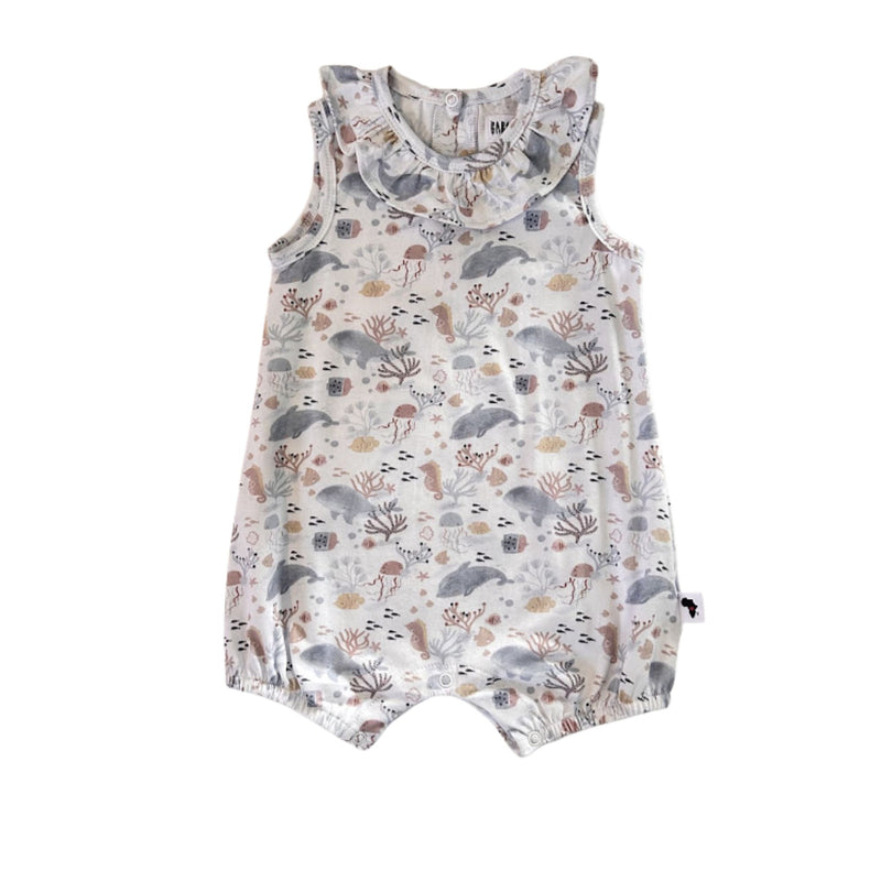 A sleeveless baby romper with a ruffled collar, featuring an all-over dolphins and sea life print in muted gray, brown, and beige tones on a white background.
