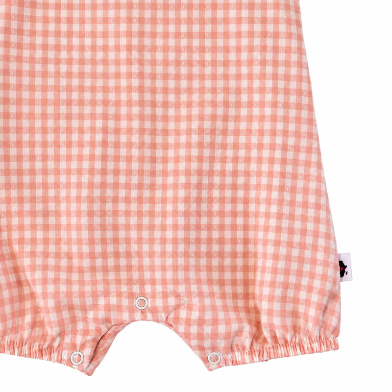 Close-up of the peach gingham Frilly Neck Romper showing white dotted fabric texture, three crotch press studs, elasticated leg openings and the side brand label.