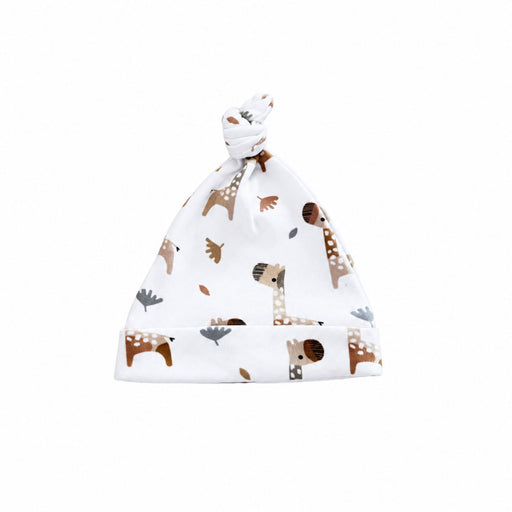White baby knot beanie featuring playful brown, beige and grey giraffes with scattered leaves, a tied top knot and wide fold-over band.