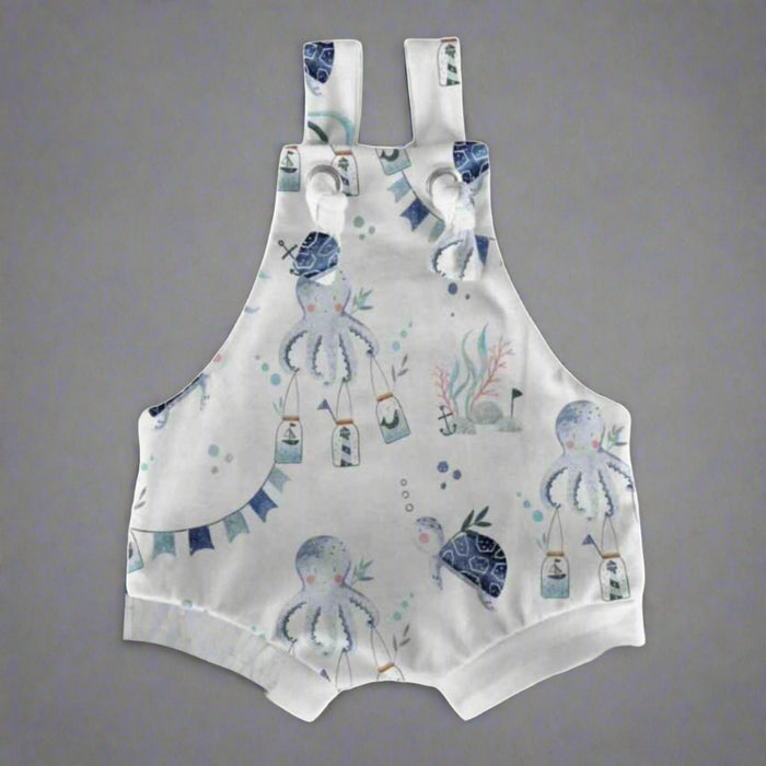 White short knot dungarees with illustrations of a playful octopus playing under the sea.