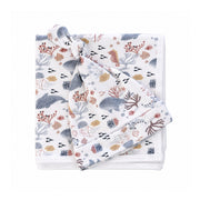 Finn and Friends knot beanie resting on a folded white baby blanket, both printed with blue-grey dolphins, pink seahorses, jellyfish and golden fish.