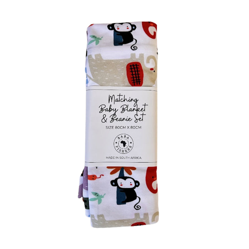 A folded matching baby blanket and beanie set wrapped in a white paper band label. The fabric features a white background with a colorful safari animal print, including a black monkey, a beige elephant, and red and blue accents.