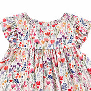 Close-up of the white floral dress’s rounded front neckline and flutter sleeves, showing delicate pink, red, purple, blue and yellow flowers with green foliage.