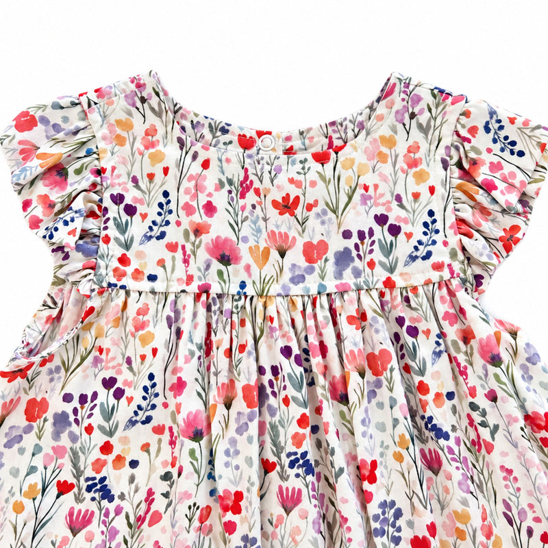 Close-up of the white floral dress’s rounded front neckline and flutter sleeves, showing delicate pink, red, purple, blue and yellow flowers with green foliage.