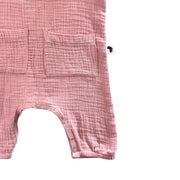Close-up of an orchid pink muslin cotton baby romper with two front patch pockets and snap closures, shown on a plain white background.