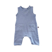 A sky blue sleeveless baby romper made of textured muslin fabric, featuring a round neckline, two front patch pockets, and legs, shown against a plain white background.