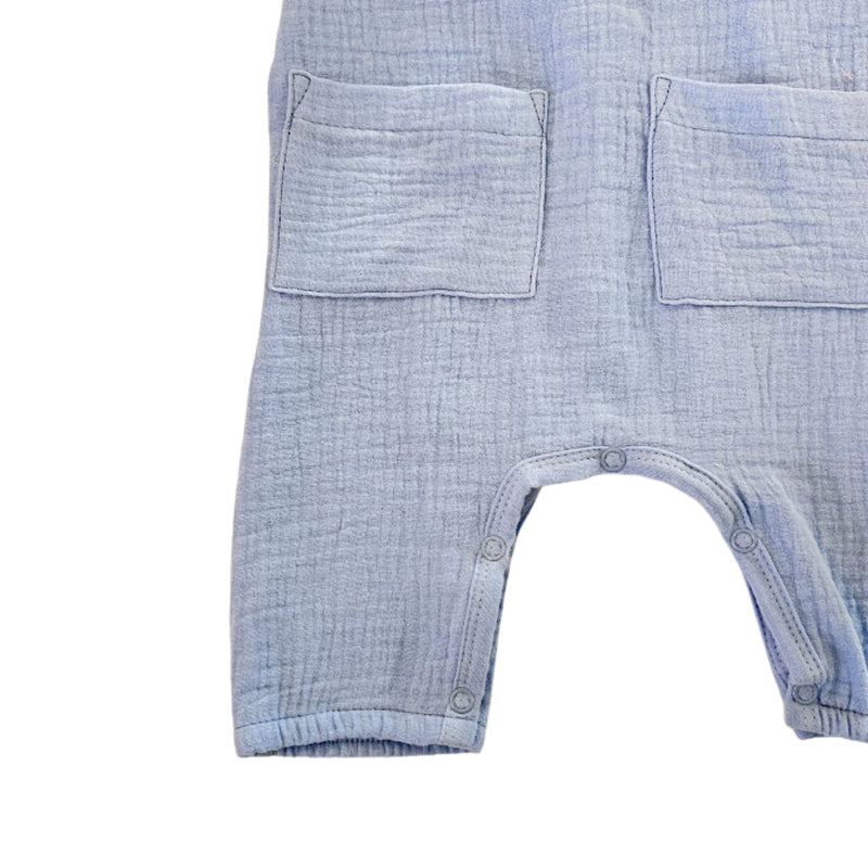 Close-up of a baby romper in skyblue muslin fabric, showing two front patch pockets and snap closures at the crotch.