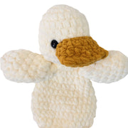 A closeup of a handmade crocheted plush duck toy with a textured cream body, mustard yellow beak, and a single black bead eye.