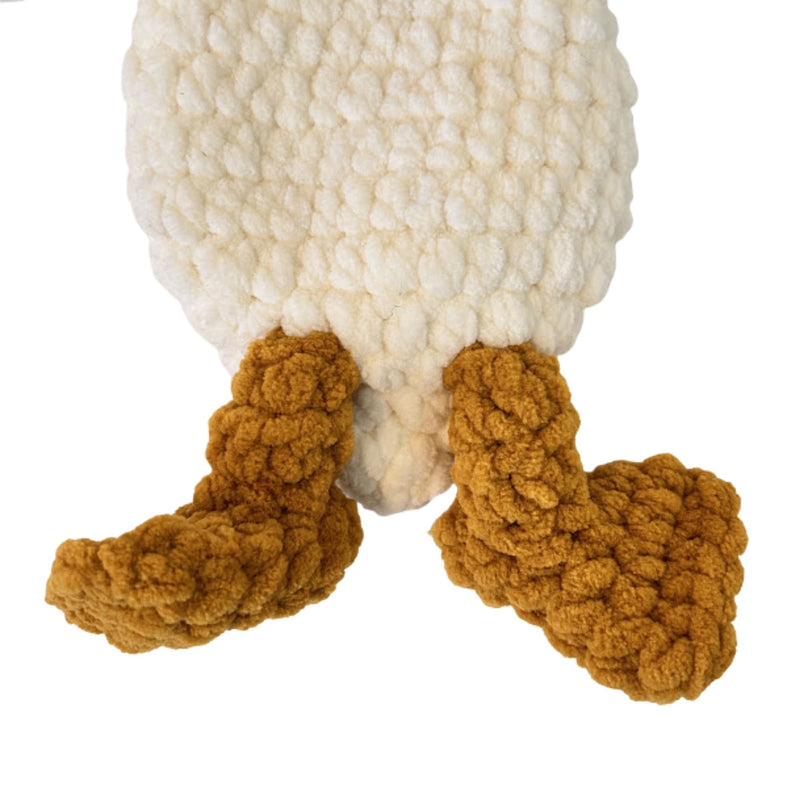 A close-up of a chunky, textured plush toy or stuffed animal showing a large cream body and two mustard-brown feet.