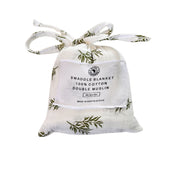 Front view of Swaddle Blanket - Wild Olive presented in a matching white muslin drawstring bag with olive-green botanical branches and fabric ties