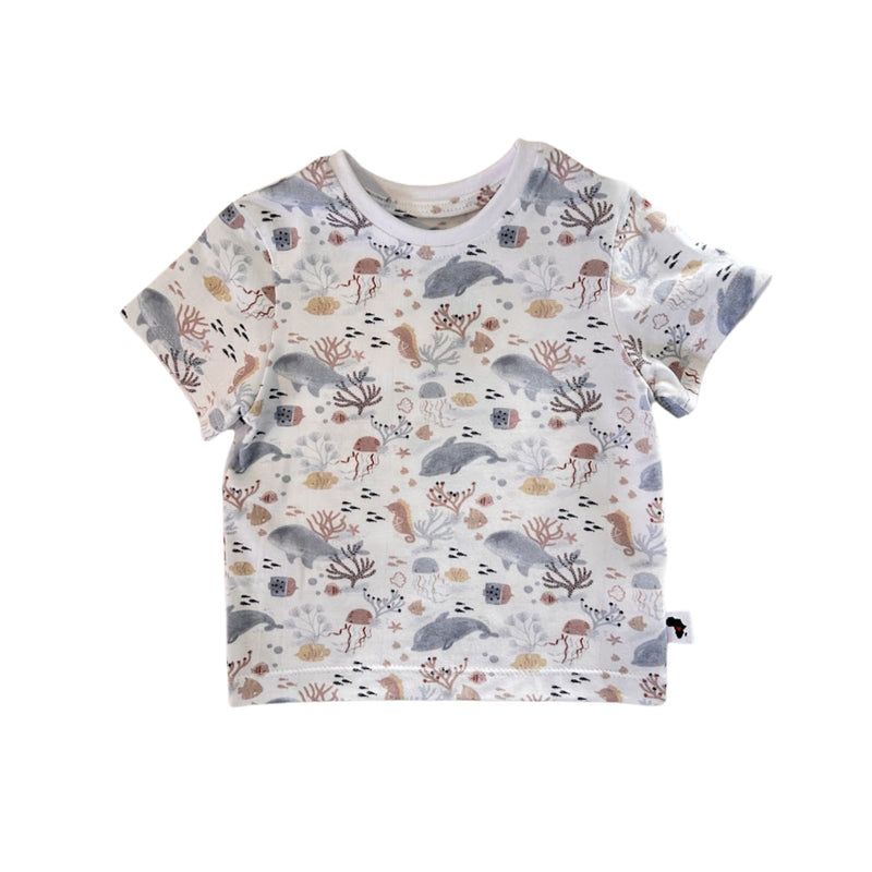A short-sleeve baby t-shirt with an all-over underwater-themed print featuring dolphins, sea anemones, starfish, and sponges in muted gray, brown, and beige tones on a white background.