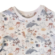 A close-up of a tee shirt with an all-over ocean-themed print featuring whales,  doplhins, seahorses, coral, jellyfish, and small fish.