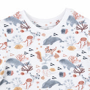 A close-up of a tee shirt with an all-over ocean-themed print featuring whales,  doplhins, seahorses, coral, jellyfish, and small fish.