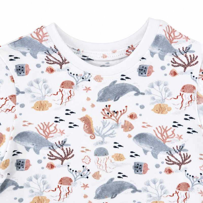 A close-up of a tee shirt with an all-over ocean-themed print featuring whales,  doplhins, seahorses, coral, jellyfish, and small fish.