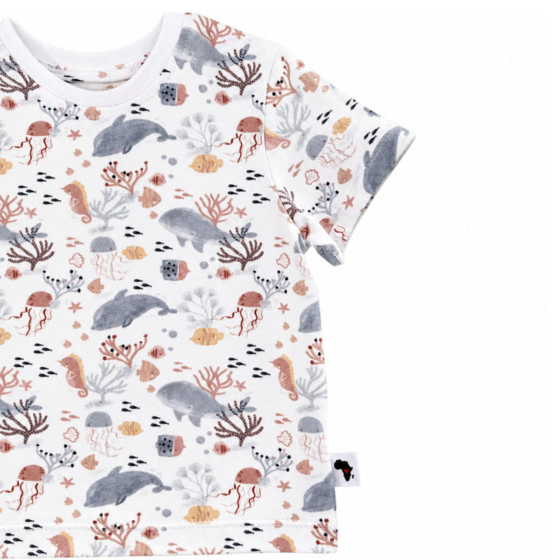 A short-sleeve child's t-shirt with an all-over underwater-themed print featuring whales, dolphins, jellyfish, seahorses, and coral in muted gray, terracotta, and beige tones.