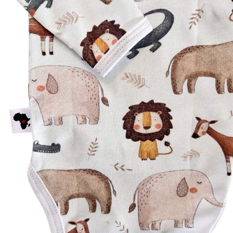 A close-up of a wrap onesie in long sleeves, featuring a playful safari animal print on an off-white background. The print includes watercolor-style elephants, lions, giraffes, a crocodile, and small leaf motifs in brown, beige, and gray tones.