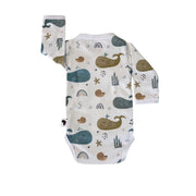 Back view of a white long-sleeve wrap-style baby onesie featuring a whimsical whale print in shades of blue, teal, and mustard, accented with rainbows, starfish, and seashells. Designed with press-stud closures for easy dressing.