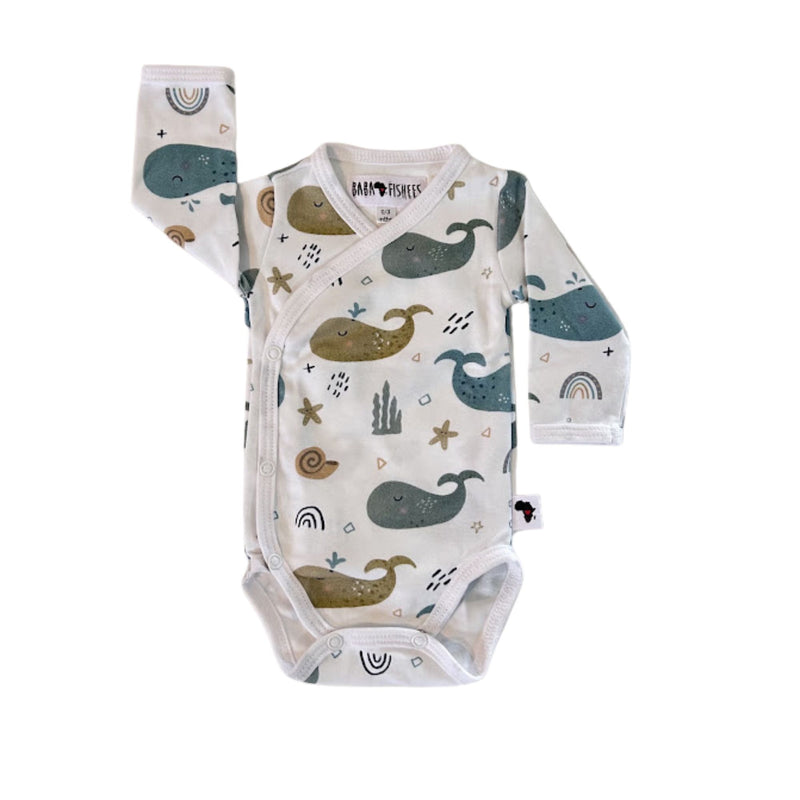 Front view of a white long-sleeve wrap-style baby onesie featuring a whimsical whale print in shades of blue, teal, and mustard, accented with rainbows, starfish, and seashells. Designed with press-stud closures for easy dressing.