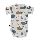 Back view of a white short-sleeve wrap-style baby onesie featuring a whimsical whale print in shades of blue, teal, and mustard, accented with rainbows, starfish, and seashells. Designed with press-stud closures for easy dressing.